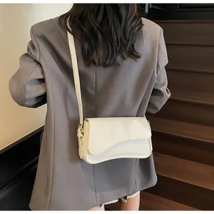 Détail du sac bandoulière crème à rabat incurvé porté par un mannequin sur un blazer