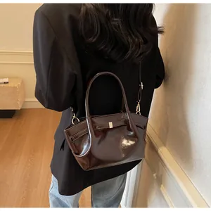 Dettagli di una borsa tote in pelle verniciata marrone scuro con finitura lucida e oro
