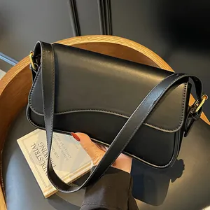 Sac bandoulière en cuir noir avec rabat magnétique et boucles dorées sur un tabouret en bois