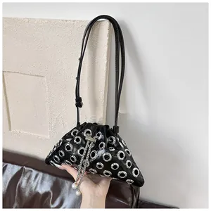 Detail of black patent leather bucket bag with silver grommets and pearl chain strap