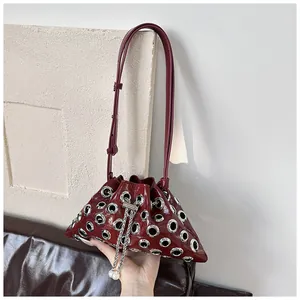 Detail view of red glossy bucket bag with silver metal eyelets and pearl chain drawstring