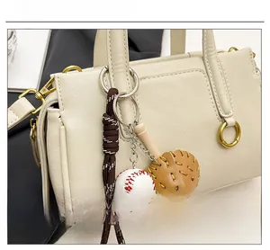 Detail of baseball charm with glove and mini bat accessory on a beige handbag