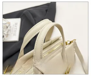 Close-up of cream leather handbag handle with gold hardware and stitching details