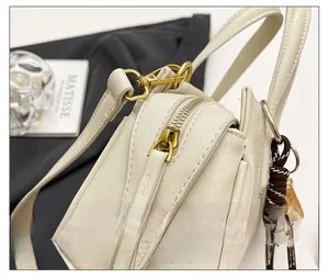 Detail of smooth gold zipper closure and baseball pendant on beige leather handbag