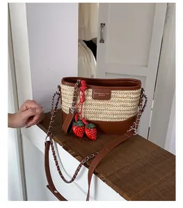 Detail der geflochtenen Strohtasche mit Lederbesatz und dekorativen Erdbeer-Anhängern