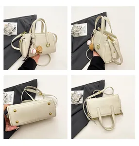 Detail view of cream handbag showing metal D-rings and baseball glove bag charm decoration