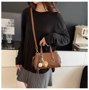Brown faux leather crossbody bag with baseball charm detail shown on a model