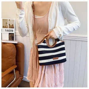 Detail of striped woven tote bag with brown leather handles and adjustable shoulder strap