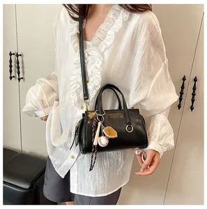Detail of a black leather handbag featuring a baseball glove and bat charm on a white shirt