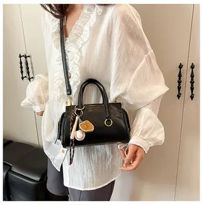Detail of black faux leather handbag with baseball charm and detachable shoulder strap