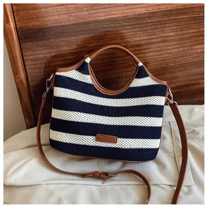 Close-up of navy striped knit tote with brown leather handles and brand label detail