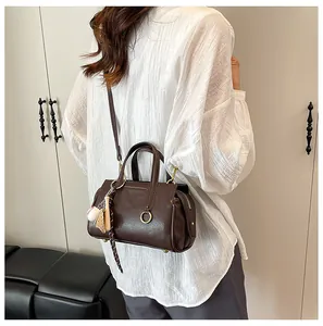 Brown vintage Boston bag detail with sports-themed charms on white textured shirt