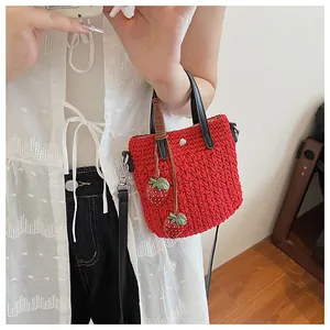 Détail d'un sac seau rouge tressé à la main avec breloques fraises 3D et bandoulière en cuir