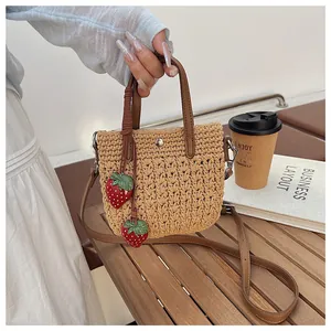 Détail du sac cabas en paille tressée avec breloques fraises et lanières en cuir brun