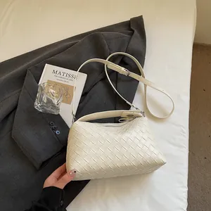 Détail du sac bandoulière en cuir tressé crème avec blazer et livre d'art
