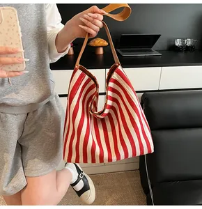 Large striped canvas tote bag with brown leather handles held by a model in a modern room