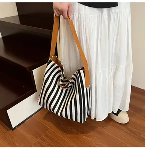 Detailed view of large striped canvas tote bag with brown leather shoulder straps