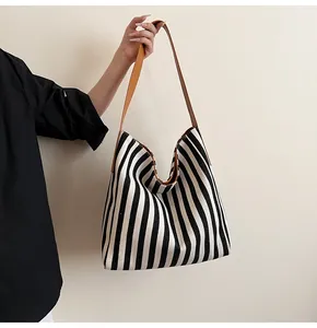 Detail of striped canvas tote bag with brown leather strap held by a person