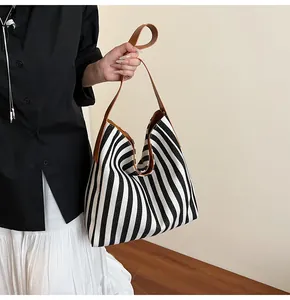 Detail of striped canvas tote with brown leather handles worn by a model against white wall