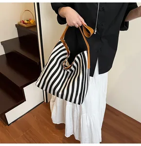 Detail of black and white striped canvas tote bag featuring brown leather shoulder straps