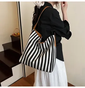 Side view of large striped canvas tote bag with brown leather strap on female model