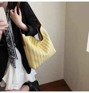 Detail of yellow and white striped canvas tote bag with brown leather shoulder straps