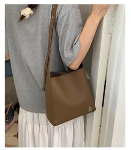 Mannequin portant un sac seau marron foncé en cuir avec logo argenté et bandoulière