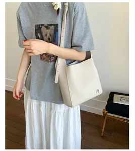 Détail du sac seau en cuir crème avec logo argenté et bandoulière réglable