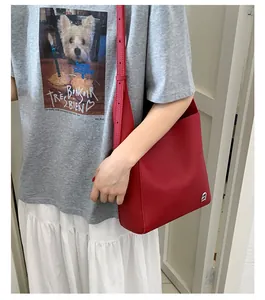 Gros plan d'un sac porté épaule rouge en cuir grainé avec bandoulière et logo en métal