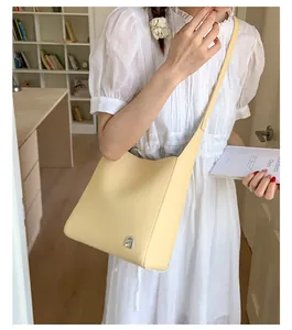 Détail du sac seau en cuir grainé avec logo argenté porté par un mannequin en intérieur