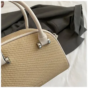 Détail d'un sac cylindre en paille beige avec poignées en cuir et boucles métalliques