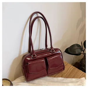 Nahaufnahme einer glänzenden weinroten Schultertasche mit zwei Vordertaschen auf einem Holztisch
