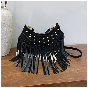 Detailed close-up of black suede crossbody bag with gold studs and bohemian tassels