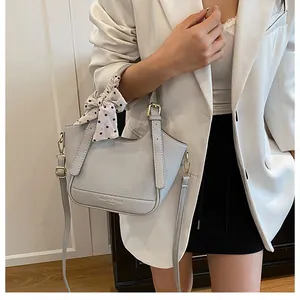 Détail d'un sac à main gris clair en cuir grainé avec nœud à pois et logo doré brillant