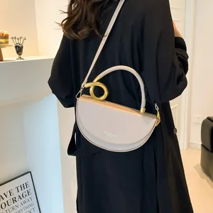 Minimalist beige moon bag with a unique gold metal handle and slim leather shoulder strap