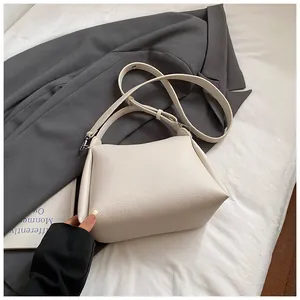 Détail du sac seau blanc cassé avec texture litchi sur un costume gris et lit