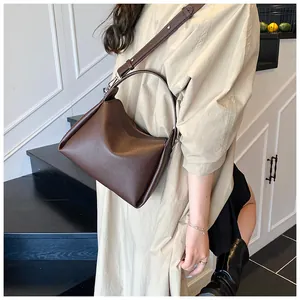 Détail du sac seau en cuir litchi marron foncé avec bandoulière réglable sur un mannequin