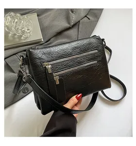 Détail du sac bandoulière en cuir noir texturé vintage avec des fermetures éclair argent