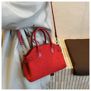 Sac à bandoulière rouge en forme de coquille porté par un mannequin en décor épuré