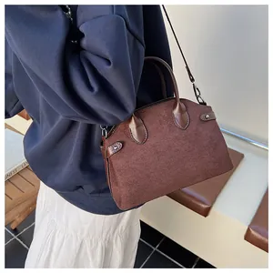 Détail du sac coquille en daim marron foncé avec poignées et bandoulière