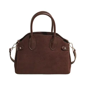 Sac à main en daim marron foncé avec poignées en cuir et bandoulière sur fond blanc