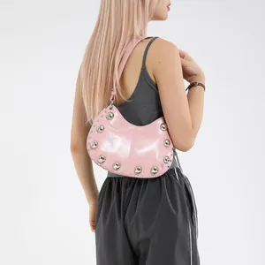 Sac demi-lune en cuir verni rose avec clous porté par un mannequin en studio