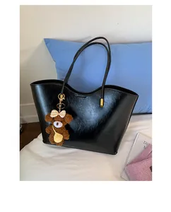 Détail du grand sac cabas noir texturé avec breloque ours en peluche sur un lit blanc