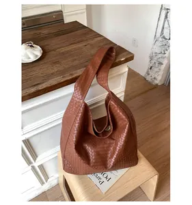 Detailed view of the brown leather hobo bag with quilted weave texture on a wooden stool