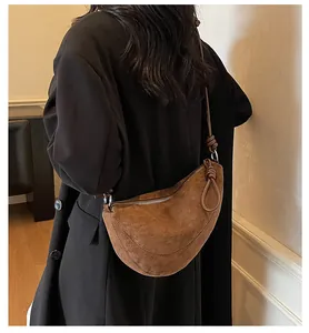 Sac demi-lune en daim marron avec bandoulière à nœud porté par un mannequin en intérieur
