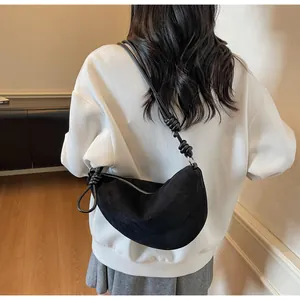 Détail d'un sac demi-lune en daim noir avec nœud sur la bandoulière porté par un modèle