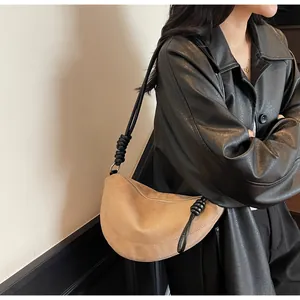 Sac bandoulière demi-lune en daim camel porté sur une veste en cuir noir tendance