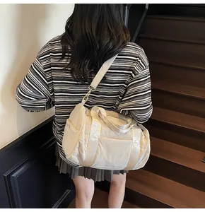 Quilted nylon duffle bag in cream white shown on model back view in staircase setting