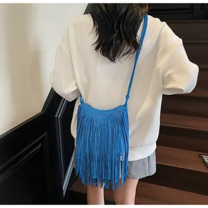 Détail d'un sac à bandoulière bleu vif avec franges porté par un mannequin en ville