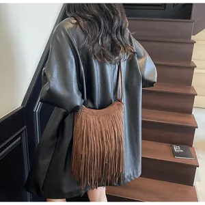 Détail du sac bandoulière marron en daim à franges bohèmes porté sur un manteau noir